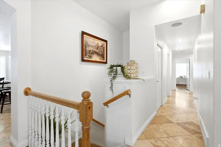 Light wood-finish staircase with white balusters, leading to a hallway with patterned tile flooring and recessed lighting