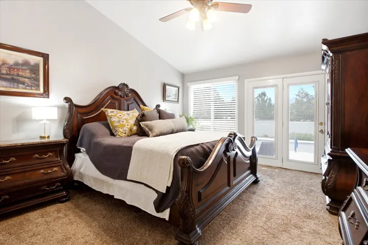 Vaulted ceiling with a ceiling fan, dual French doors, large window with blinds, and carpeted flooring