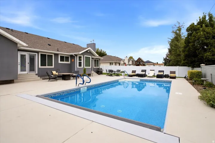 Rectangular in-ground swimming pool with surrounding concrete patio, white privacy fencing, and exterior stucco finish