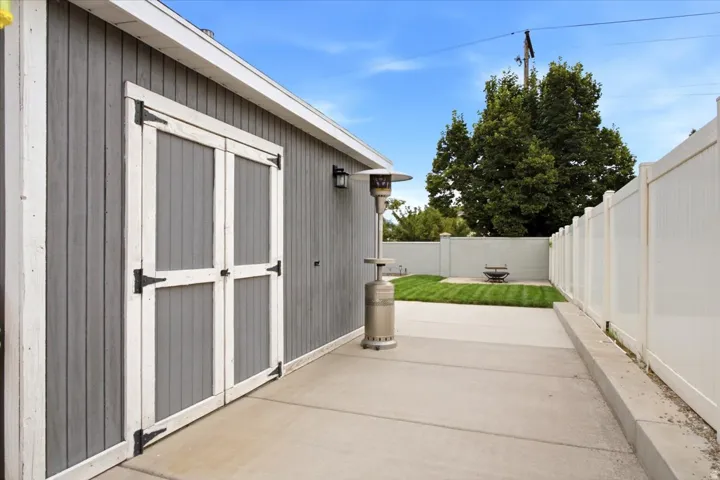 Concrete patio with a manicured lawn, white privacy fencing, and exterior wall sconce lighting
