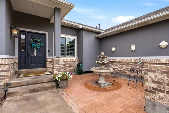 Front entry with a dark gray door, covered porch, exterior lighting, and concrete steps