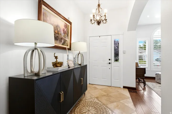 White double entry door with a sidelight, an ornate chandelier, arched doorway, wood-finish flooring, and tile flooring with a decorative inlay