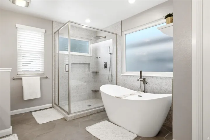 Freestanding soaking tub, glass-enclosed shower with rain showerhead, mosaic tile shower, and heated tile flooring