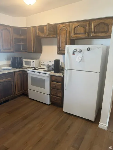 Kitchen featuring wood-finish cabinetry, white appliances, and wood-finish flooring