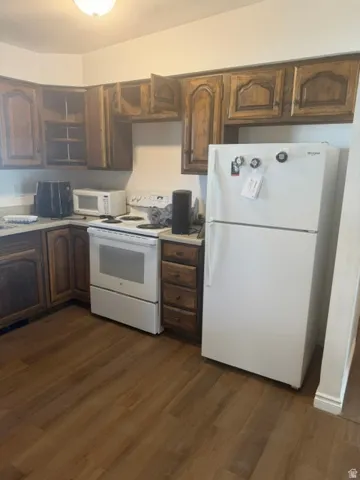 Kitchen featuring wood-finish cabinetry, white appliances, and wood-finish flooring