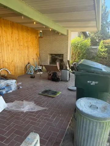Brick flooring in a herringbone pattern, wood-paneled wall, brick fireplace with a raised hearth, and a covered patio area