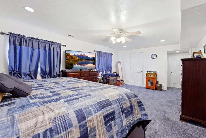 Spacious primary bedroom suite featuring wall-to-wall carpeting, dual bed configurations, ceiling fan with integrated lighting, large windows with blue drapery, ample natural light, and substantial closet storage