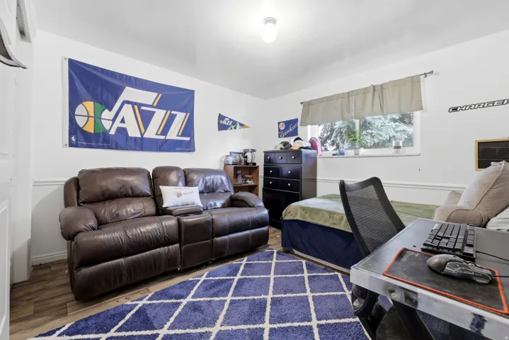 Bedroom featuring hardwood flooring, a brown leather reclining sectional, built-in dark wood cabinetry, a geometric area rug in navy and cream tones, a black mesh desk chair, and a work desk with integrated storage