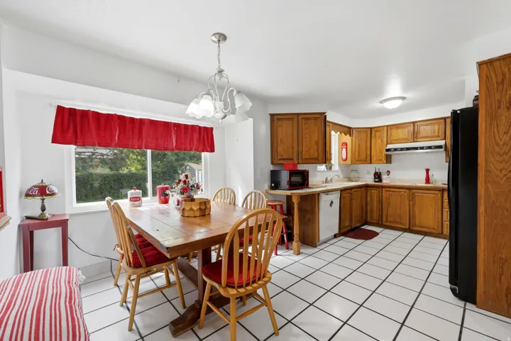 Bright kitchen and dining area featuring wood-finish cabinetry, tile flooring, stainless steel appliances, and a pendant light fixture