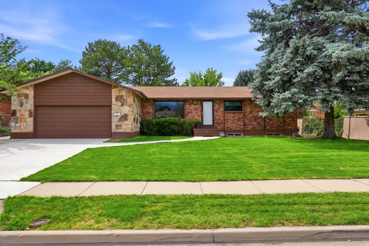 Brick and stone exterior featuring an attached garage, paved driveway, and mature landscaping