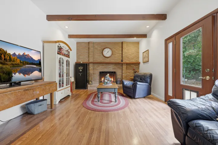Exposed beam ceiling, brick fireplace, wood-finish flooring, recessed lighting, and a glass-paneled exterior door