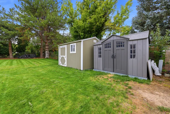 Expansive lawn area, two outdoor storage sheds, and mature perimeter trees