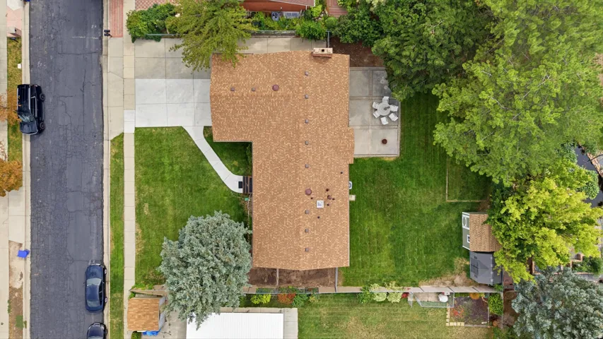 Expansive residential property featuring a large shingle roof, concrete driveway, front lawn, backyard patio, and additional storage shed