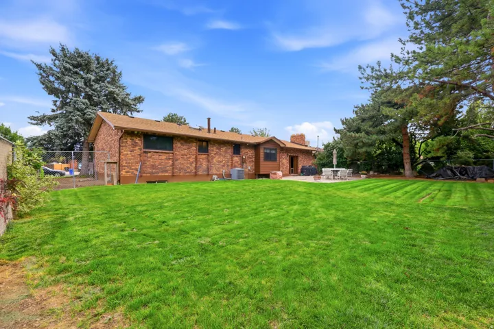 Expansive manicured lawn with mature tree-lined perimeter and brick construction residence featuring multiple windows and chimney detail