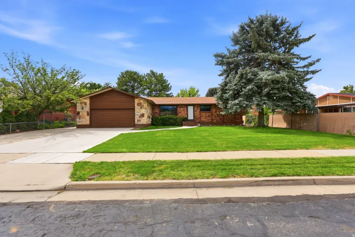 Stone and brick facade with a prominent front lawn, a driveway, and an attached garage