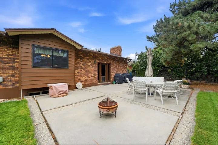 Expansive concrete patio with integrated fire pit, bordered by mature landscaping and manicured lawn