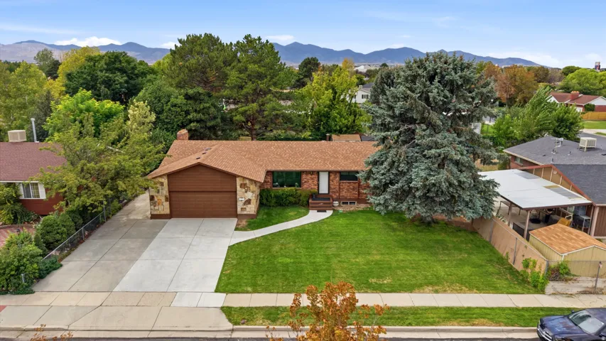 Stone veneer facade, attached garage, concrete driveway, mature landscaping, manicured lawn