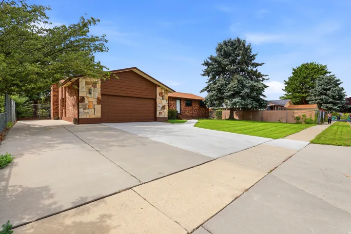 Concrete driveway, attached garage, stone veneer accents, brick siding, mature landscaping
