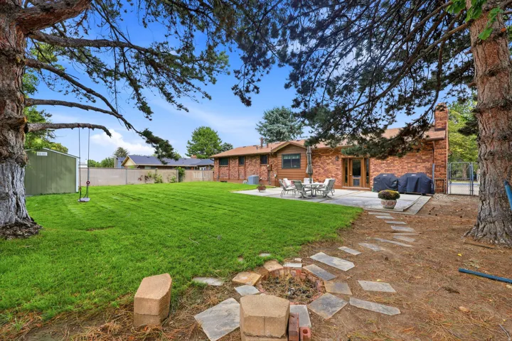 Expansive backyard featuring a manicured lawn, brick exterior, paved patio, and a stone fire pit