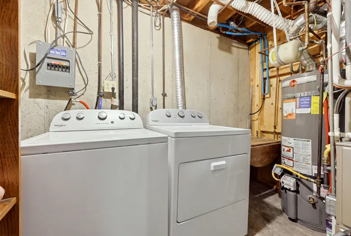Laundry area with a washer and dryer, adjacent to a water heater, with exposed ceiling joists and utility piping