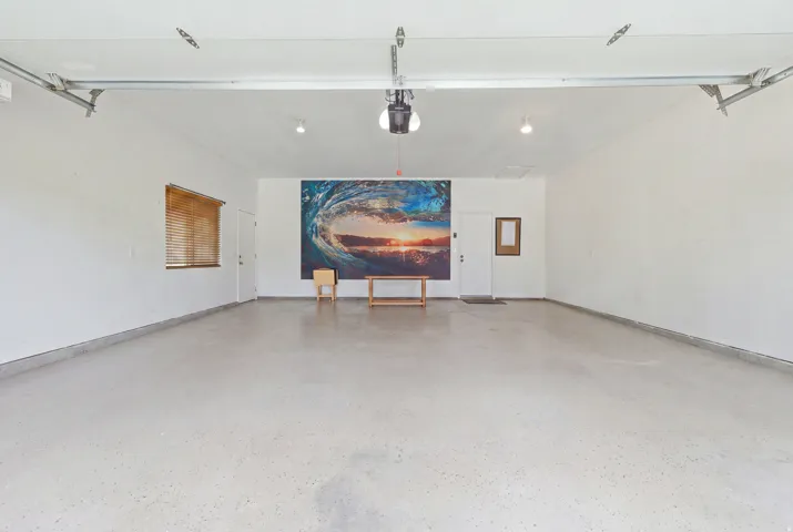Spacious garage featuring a light-colored finished concrete floor, white walls, two entry doors, and a window with horizontal blinds