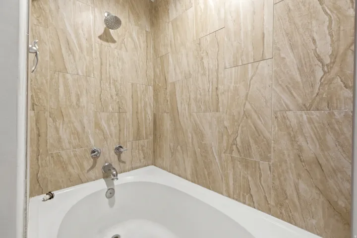 Bathtub with a tiled surround, chrome showerhead, and matching chrome fixtures