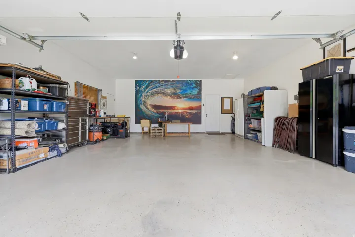 Spacious garage featuring polished concrete flooring, overhead track lighting, wall-mounted shelving and storage systems, and a garage door opener