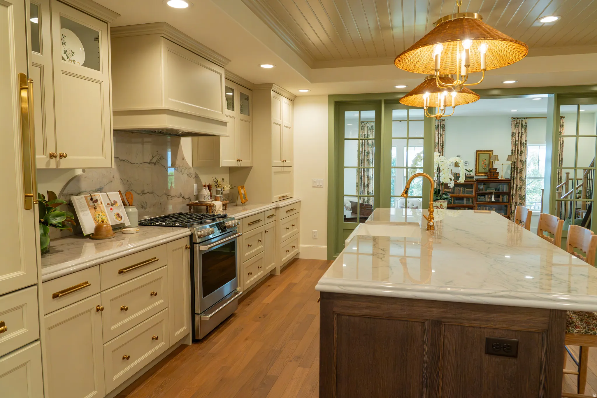 Kitchen featuring a large island with a stone countertop, brass faucet, built-in stainless steel range, and paneled cabinetry