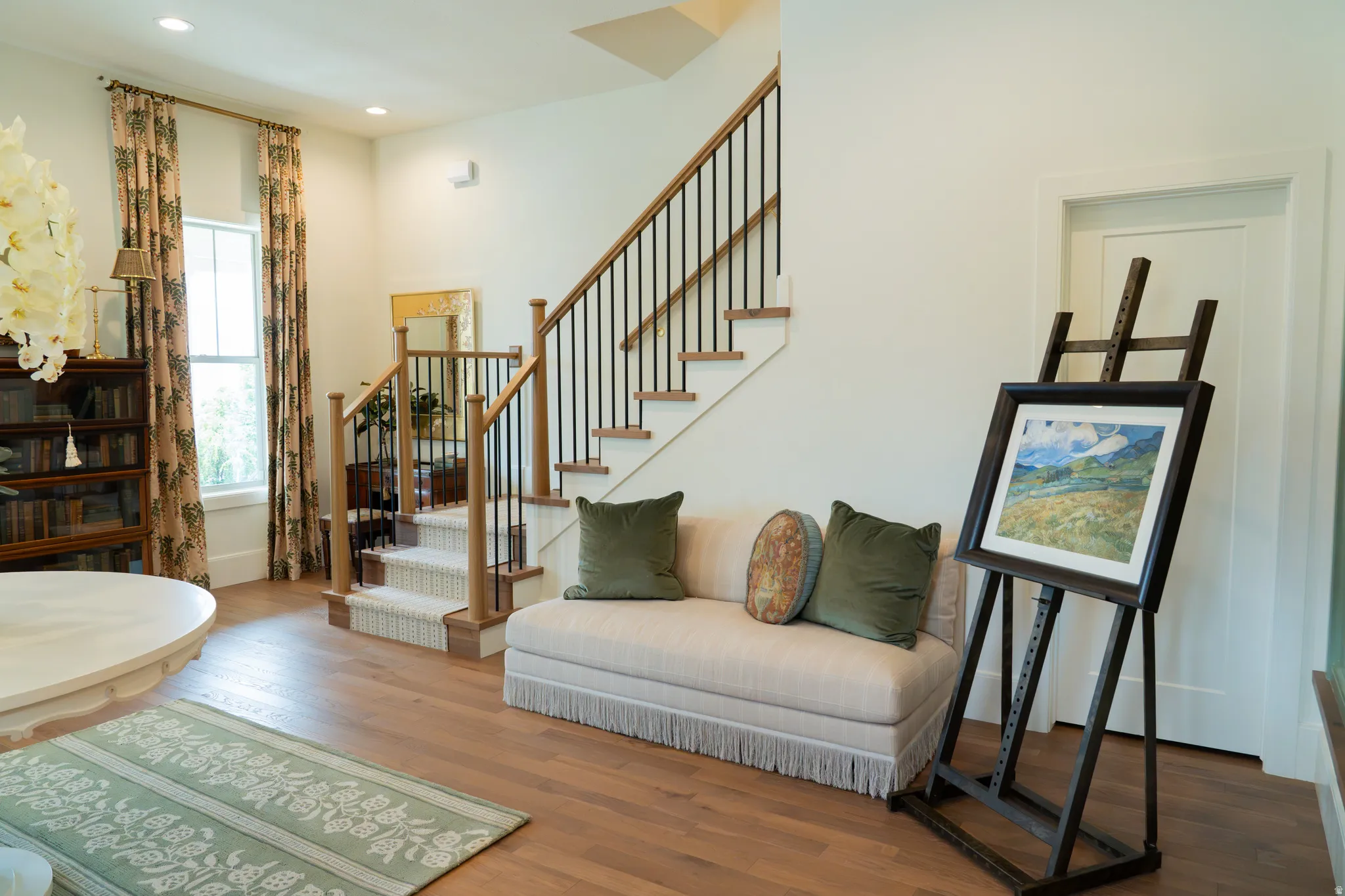 Hardwood flooring, white walls, wood staircase with black iron spindles, built-in bookshelf, recessed lighting