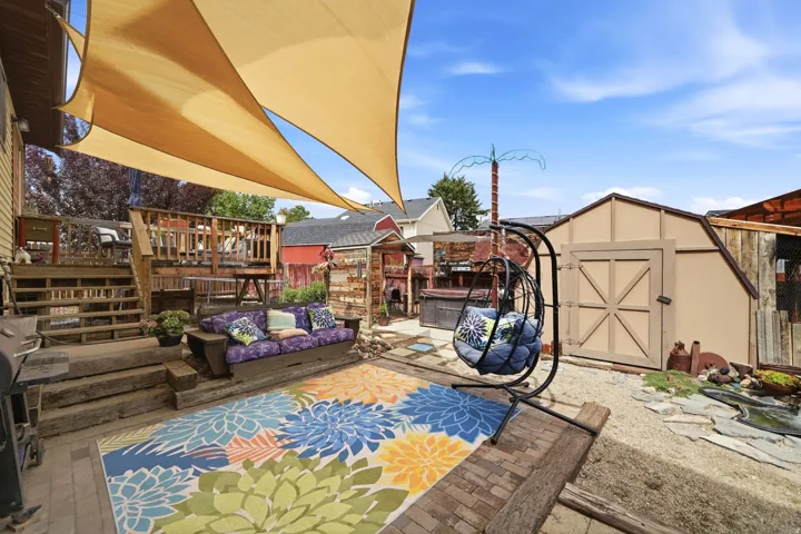 Tiered wooden deck with steps, overhead shade sails, and a detached storage shed