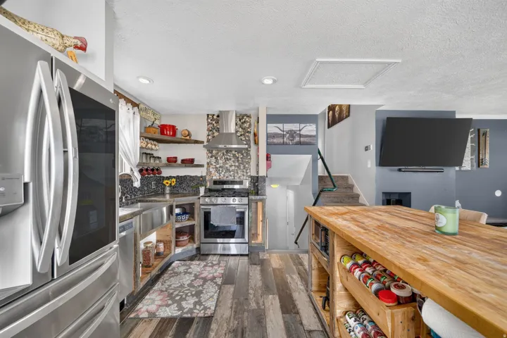 Stainless steel French door refrigerator, stainless steel kitchen appliances, wood-finish flooring, staircase with dark handrail, and a built-in television