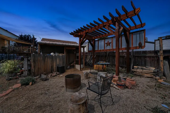 Wood pergola structure, gravel ground cover, wood privacy fencing, and an outbuilding with a corrugated metal roof
