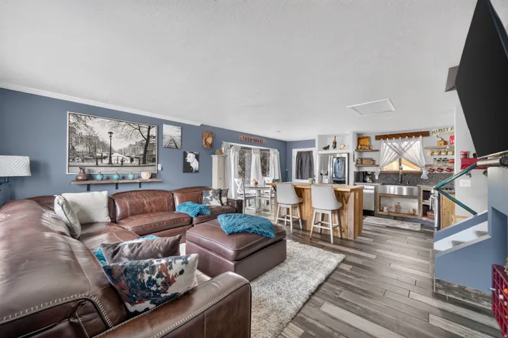 Open concept living area with wood-finish flooring, a kitchen island with seating, a stainless steel farmhouse sink, and open shelving