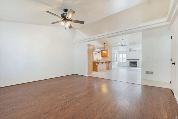 Wood-finish flooring, ceiling fan with integrated lighting, framed entryway, white paneled door with matte black hardware, and an open concept layout