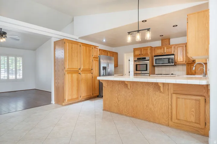 Kitchen featuring wood cabinetry, stainless steel appliances, a tiled countertop, and a built-in breakfast bar