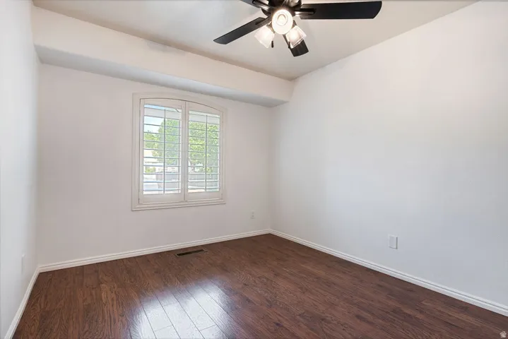 Wood-finish flooring, white walls, arched window with plantation shutters, and a ceiling fan with integrated lighting