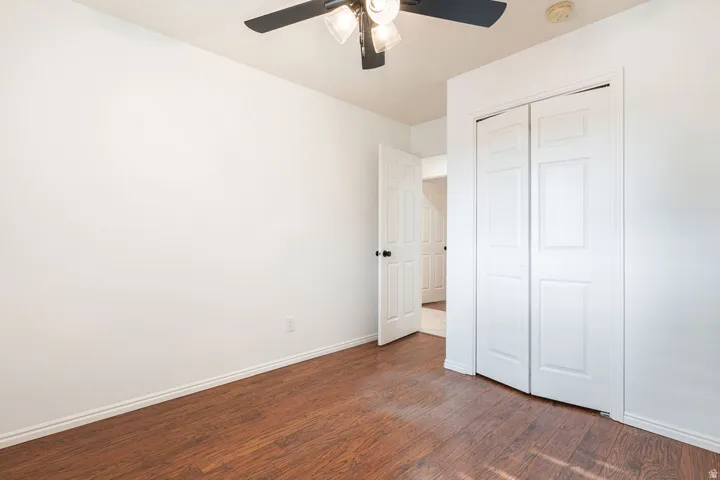Wood-finish flooring, white walls, white bi-fold closet doors, and an overhead ceiling fan with light fixture