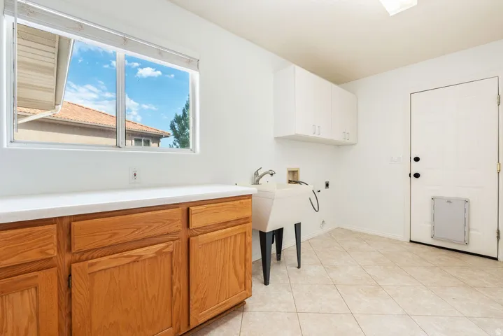 Utility room featuring a window, wood cabinetry, white countertops, a utility sink, and overhead storage