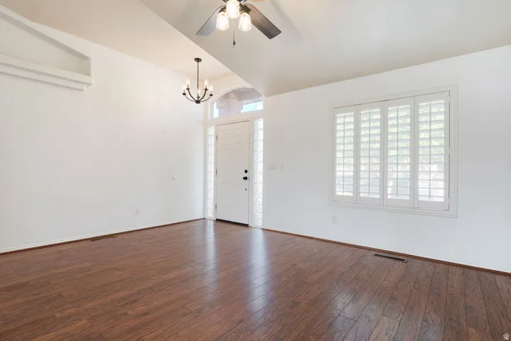 Vaulted ceiling with exposed beam, wood-finish flooring, white plantation shutters, glass block sidelights, and a ceiling fan with integrated lighting