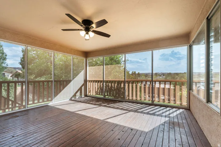 Enclosed outdoor living space featuring wood-finish flooring, a ceiling fan with integrated lighting, and multiple large windows