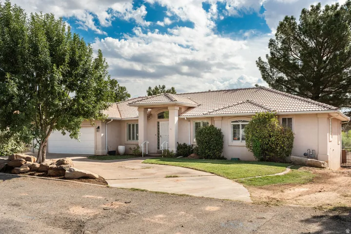 Stucco exterior with a tiled roof, featuring a two-car garage, a paved driveway, and manicured landscaping