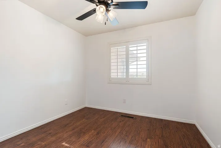 Wood-finish flooring with white trim, white walls, and a window with white plantation shutters