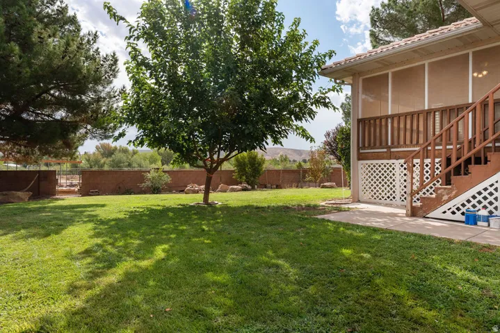 Expansive grassy yard with mature trees, offering a screened-in porch with wood railings, and a concrete patio