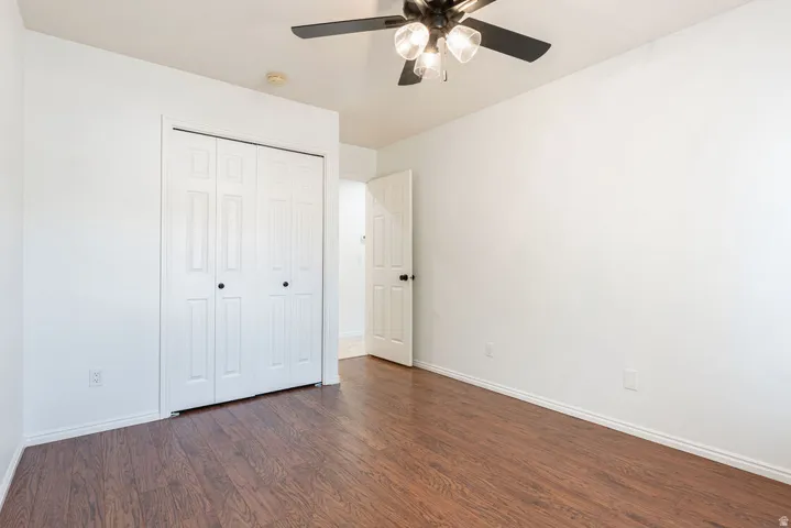 Wood-finish flooring, white walls, bi-fold closet doors with black hardware, white interior door with black hardware, and a ceiling fan with integrated lighting