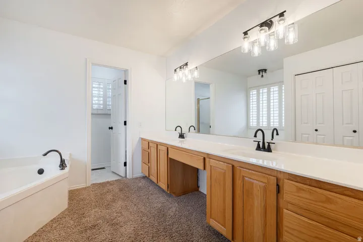Dual vanity with wood-finish cabinetry and white countertops, featuring matte black faucets and a built-in bathtub with a matching faucet