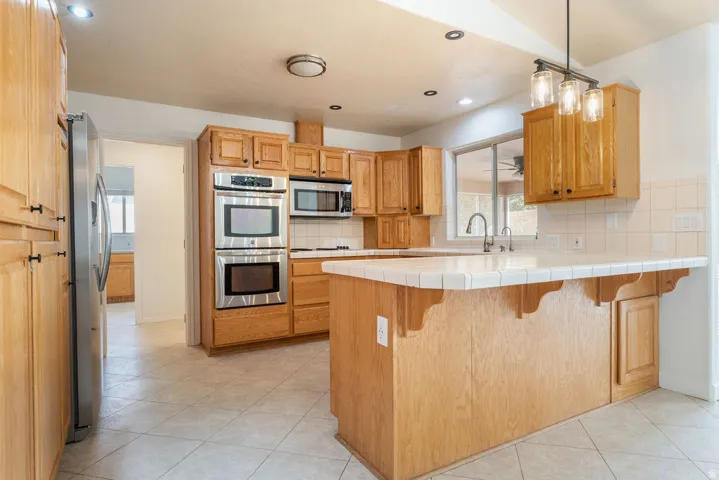 Kitchen featuring wood cabinetry, stainless steel appliances, tile countertops, tile flooring, and a kitchen island with a breakfast bar