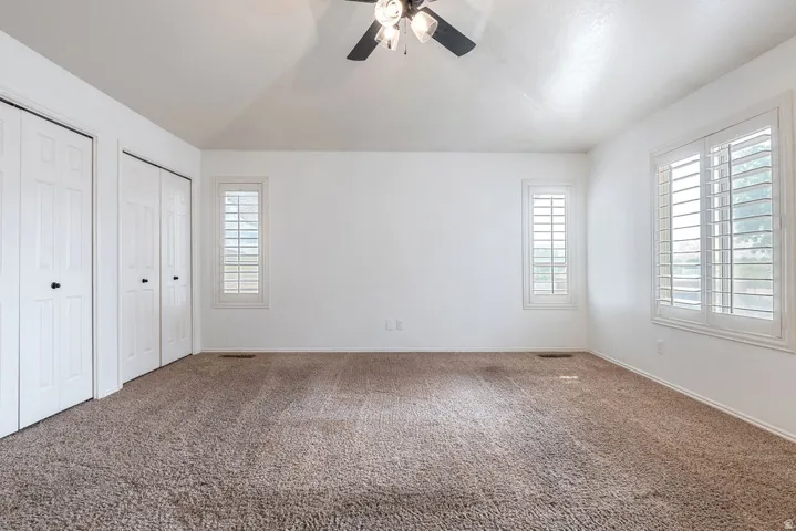 Recessed closet doors with black hardware, neutral tone carpeting, and multiple windows with white plantation shutters