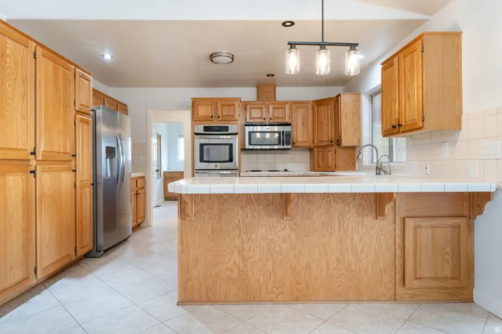 Kitchen featuring wood cabinetry, stainless steel appliances, tile flooring, and a breakfast bar with tile countertop
