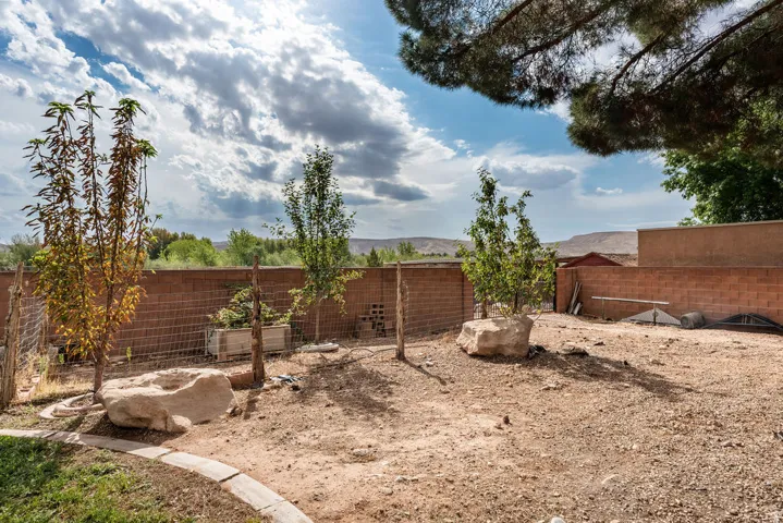 Expansive backyard with a surrounding brick privacy wall, established trees, and natural rock accents