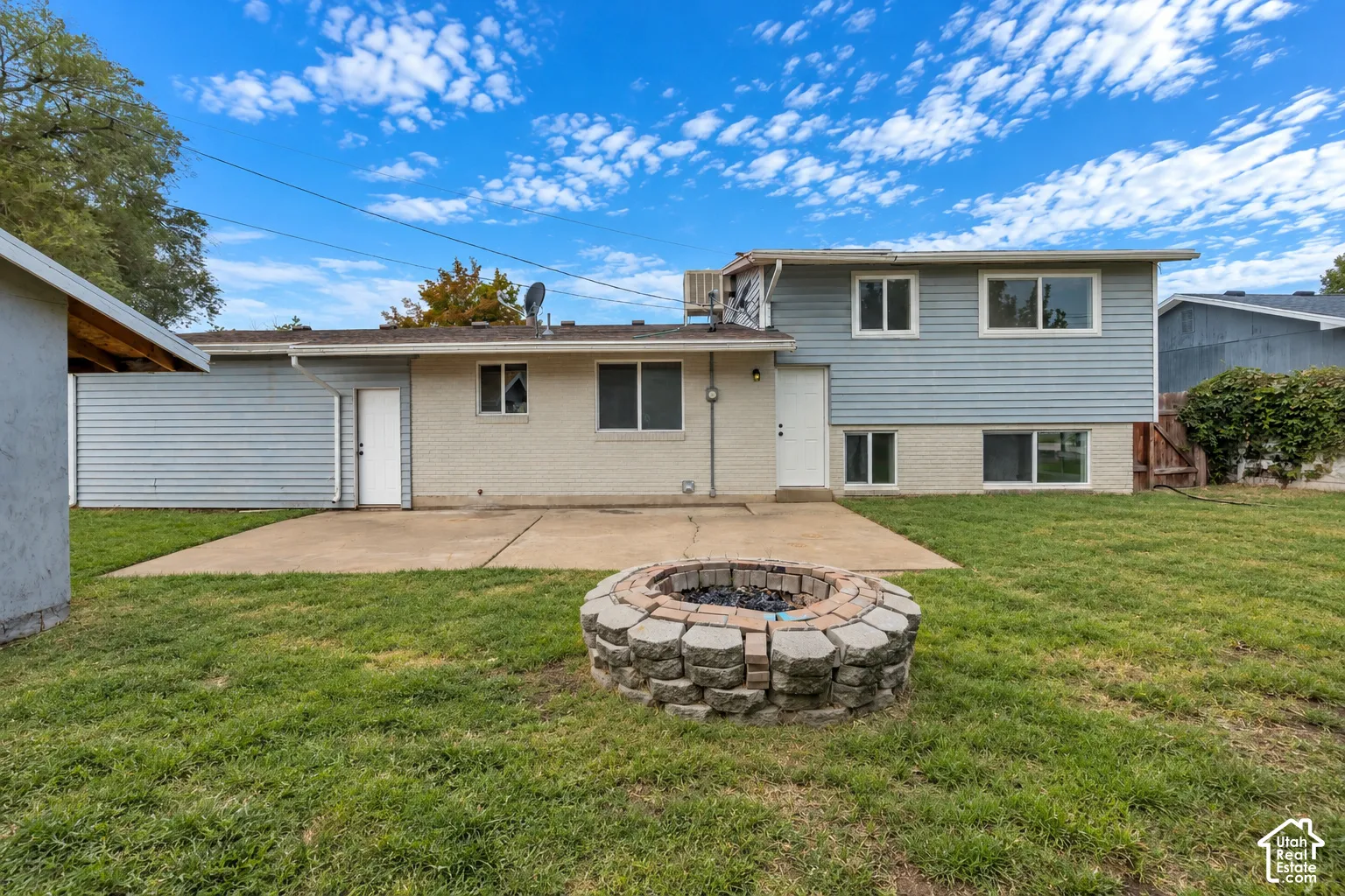 Backyard featuring a concrete patio, stone-block fire pit, and grass lawn
